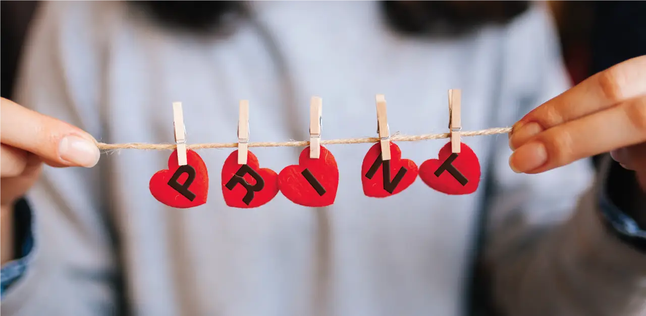 A woman holding a string with hearts clipped to it that spell out the word 'print'