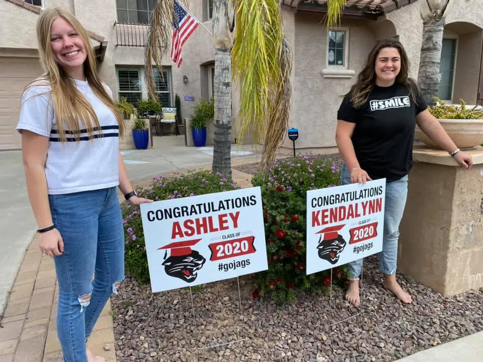 Two high school graduates standing next to yard signs