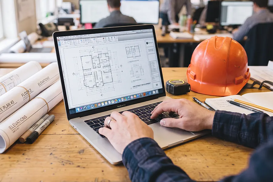 Closeup of a man using a laptop with construction plans on the screen